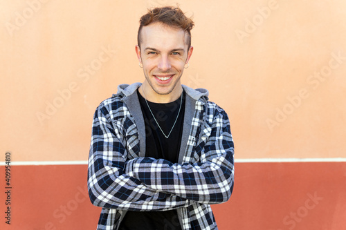 Positive confident young hipster guy in casual checkered shirt looking at camera and smiling while standing against orange wall