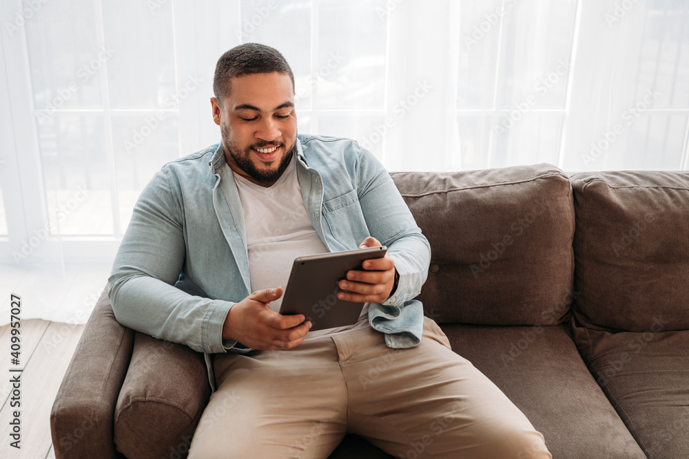 Smiling man with digital tablet sitting on a sofa at home Smiling man with digital tablet sitting on a sofa at home