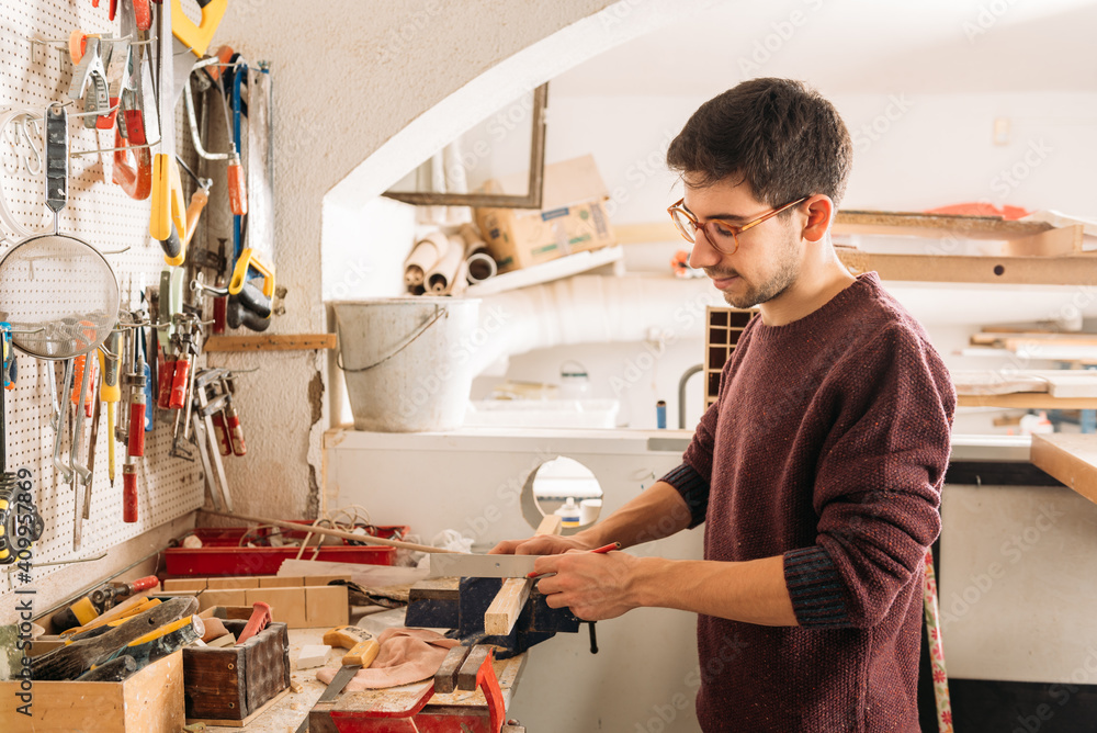 Side view of crop faceless male carpenter using metal angle and wooden plank while working at workbench in bright garage Side view of crop faceless male carpenter using metal angle and wooden plank while working at workbench in bright garage
