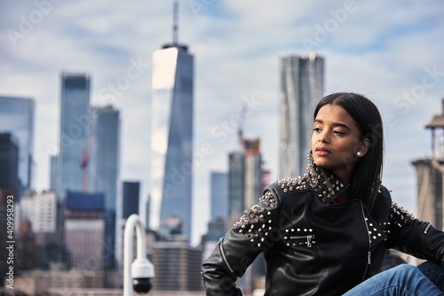 Thoughtful African American female in leather jacket sitting on street in New York and enjoying cityscape photo