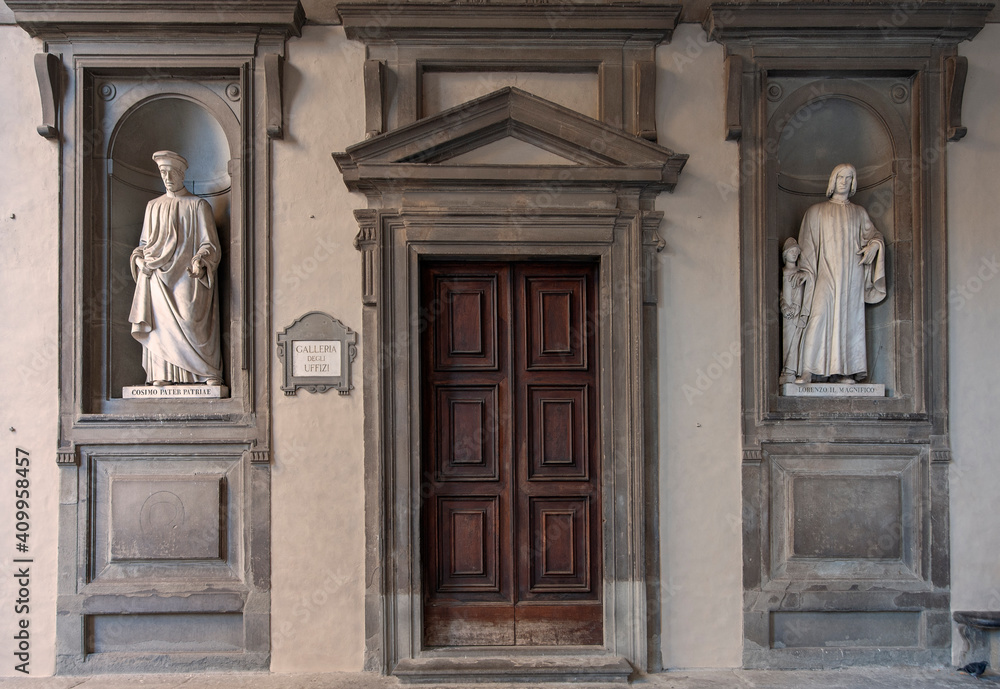Florence, Italy - 2020, January 18: Old wooden entry door to the Uffizi Gallery Museum. Cosimo and Lorenzo Medici marble statues on either side..
