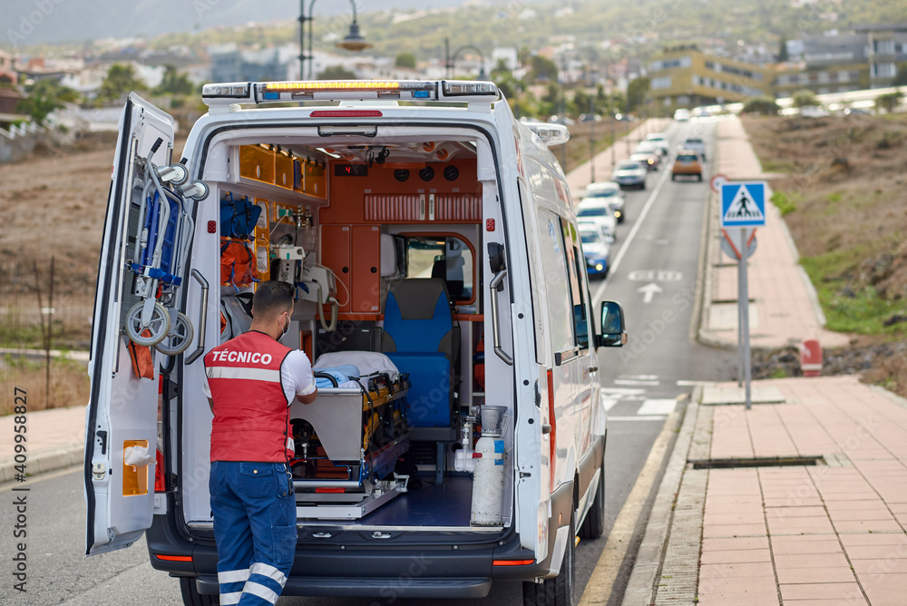 Back view of professional male paramedic in protective mask pulling stretcher out of ambulance van parked on street Back view of professional male paramedic in protective mask pulling stretcher out of ambulance van parked on street