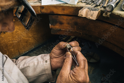 Side view of crop unrecognizable male goldsmith in glasses holding tweezers with diamond while creating jewelry accessory at workbench