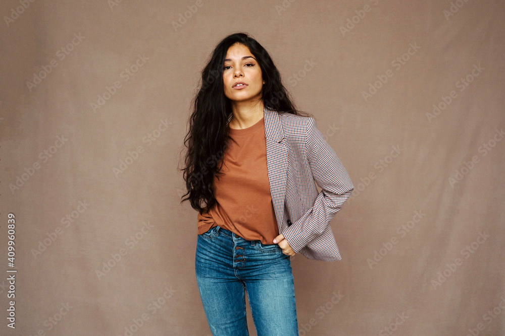 Ethnic female in casual jacket looking at camera standing on brown background in studio Ethnic female in casual jacket looking at camera standing on brown background in studio
