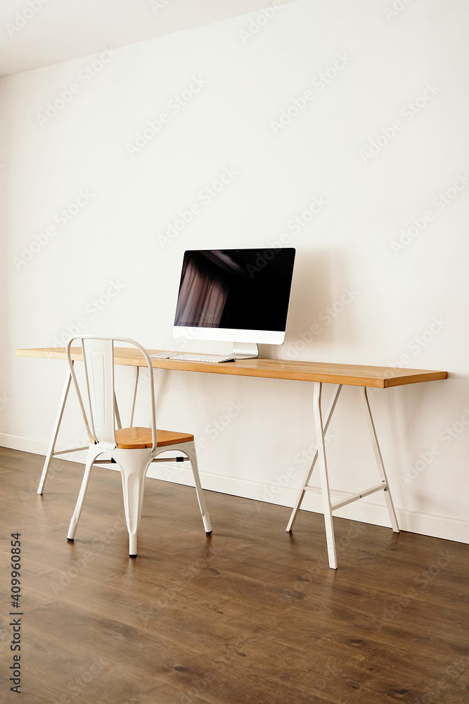 Modern computer placed on wooden table near chair in contemporary light room with minimalist interior Modern computer placed on wooden table near chair in contemporary light room with minimalist interior