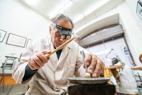 Low angle of focused skilled mature male master in glasses using hammer and chisel while working with gemstone in jewelry workshop photo
