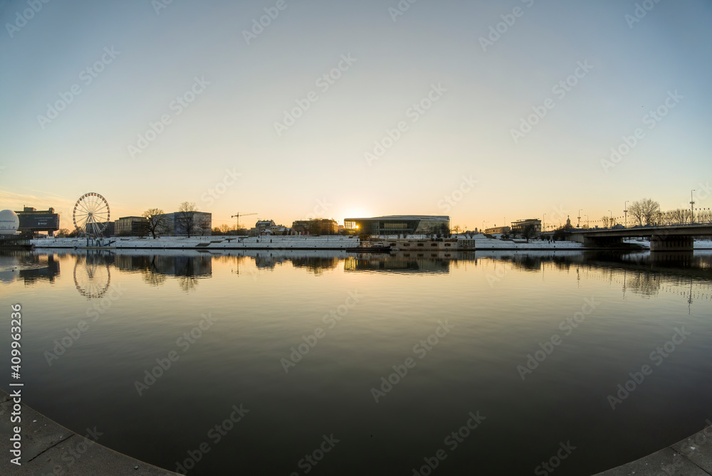 Krakow, South Poland - January 31, 2021: Pan shot of Vistula river against polish building located at the center of the city during peaceful sunset sunrise in winter. Krakow cityscape