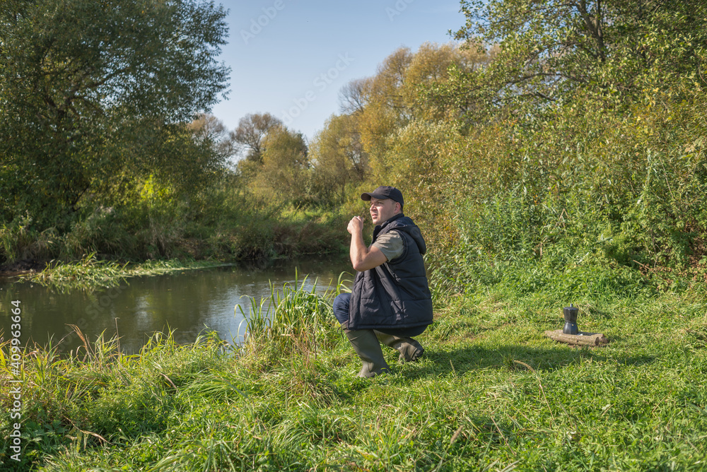 Young man with a mug sits in nature near the river. Young man with a mug sits in nature near the river.