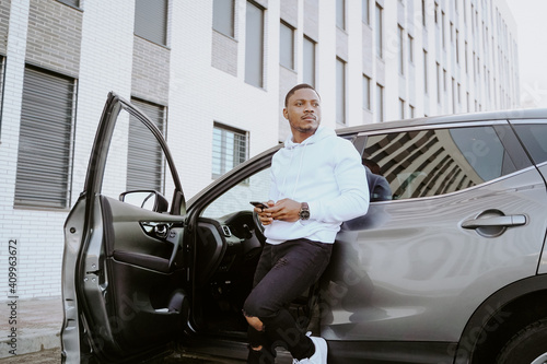 African American male standing near expensive car and surfing Internet on smartphone photo