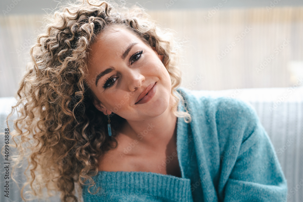 Coquette female with curly hair and in warm knitted sweater resting on comfortable sofa and looking at camera Coquette female with curly hair and in warm knitted sweater resting on comfortable sofa and looking at camera