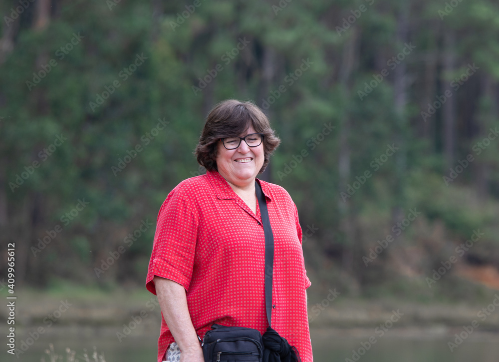 Fototapeta premium portrait of a pretty smiling middle aged woman on a wild beach surrounded by trees 