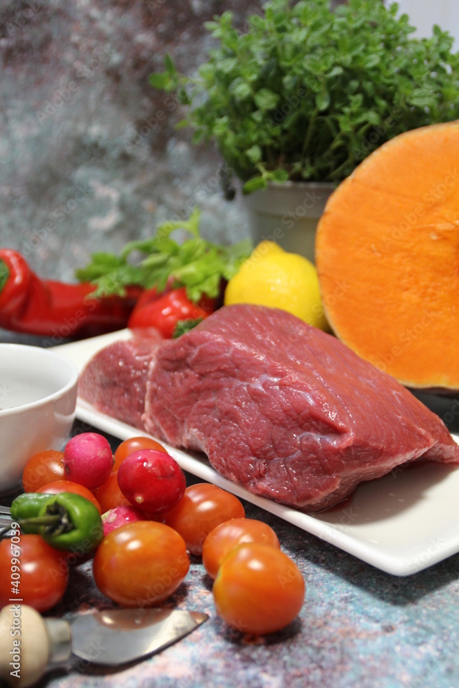 a piece of beef on a plate, colorful vegetables, tomatoes, peppers and large orange pumpkins cut in half