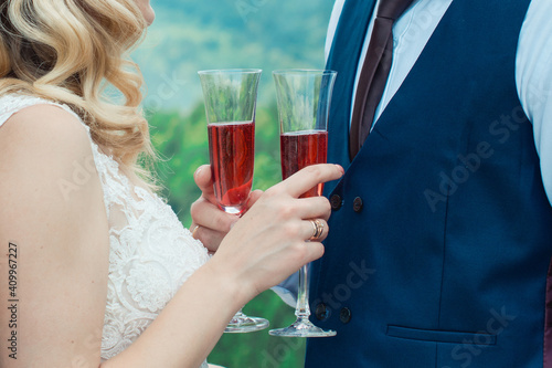Glasses with red champagne drink in bride and groom hands. Happy newlyweds drinking. Loving couple created new family. photo