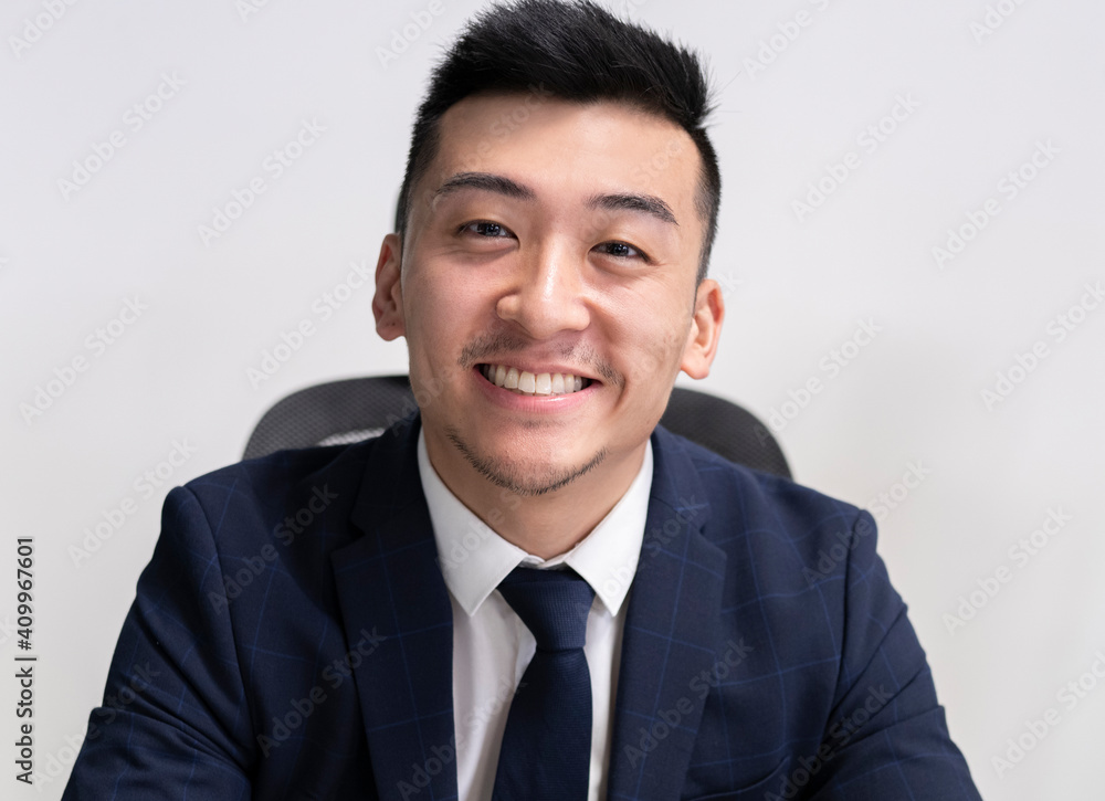 Positive young Asian male executive manager in business style wear looking at camera while sitting in office Positive young Asian male executive manager in business style wear looking at camera while sitting in office