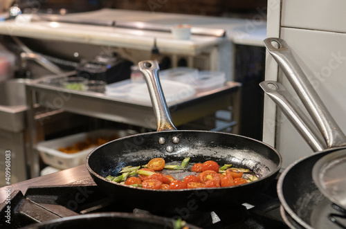 Skillet pan with fried tomatoes and greens placed on stove in modern restaurant kitchen during meal preparation photo