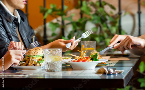 Group of crop anonymous friends gathering at table with various snacks and drinks while having dinner together in cozy restaurant photo