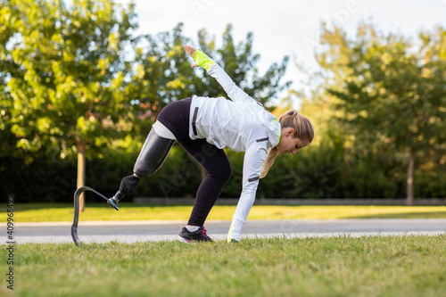 Side view of professional female runner with leg prosthesis preparing for explosive start during training in park photo