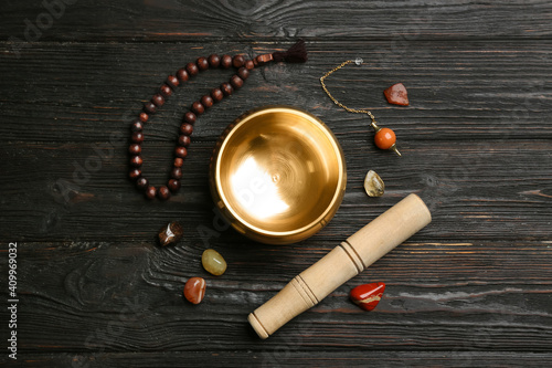 Flat lay composition with golden singing bowl on black wooden table. Sound healing