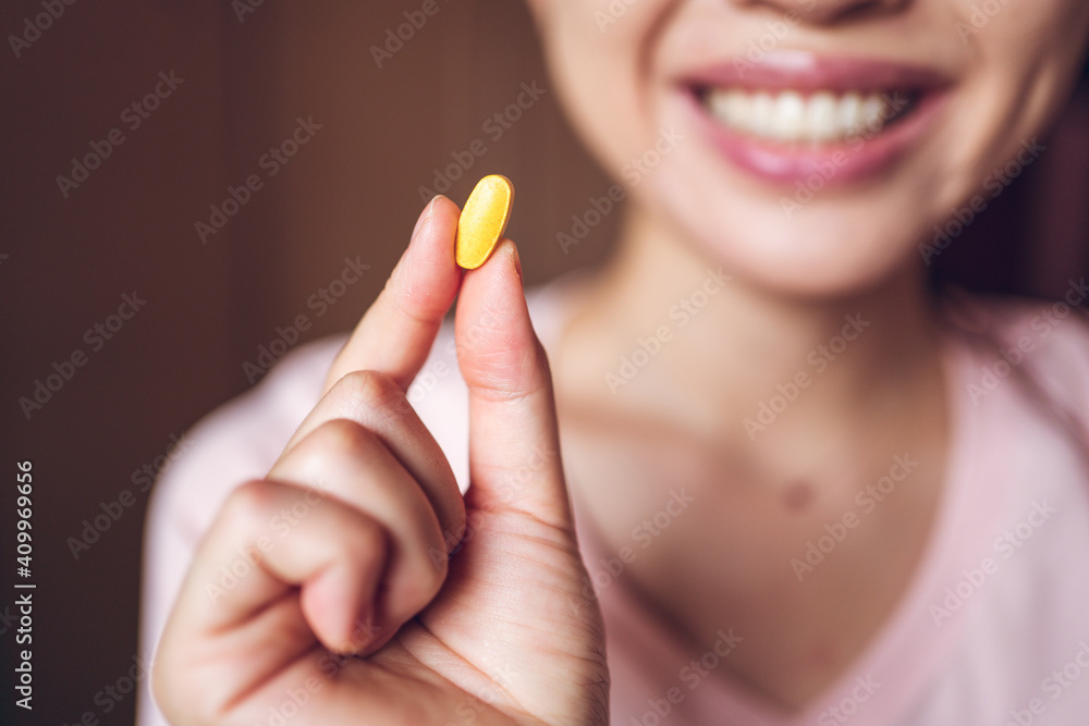 Crop unrecognizable cheerful healthy female showing bright yellow vitamin pill during health care routine at home Crop unrecognizable cheerful healthy female showing bright yellow vitamin pill during health care routine at home