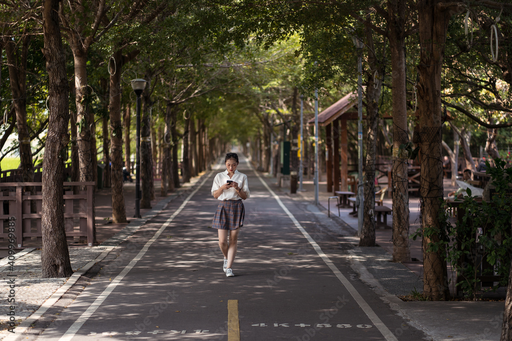 Ethnic Asian female using smartphone and walking along Tanya Shen Green Bikeway in Taichung Ethnic Asian female using smartphone and walking along Tanya Shen Green Bikeway in Taichung
