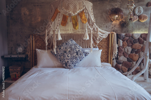 Comfortable bed with white linen and ornamental cushion in hotel room with natural stone walls and hanging rope decoration in Taiwan photo