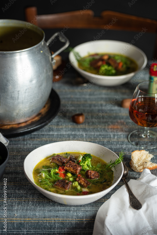 High angle of palatable hot soup with green herbs and meat served with glass of cognac on rustic table High angle of palatable hot soup with green herbs and meat served with glass of cognac on rustic table
