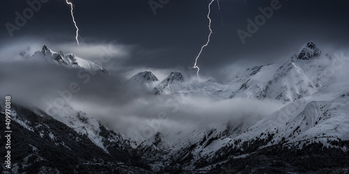 Scenery of mountain range covered with snow under thunderstorm sky with bright lightnings in winter photo