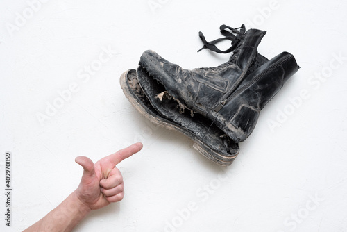 Male hand is showing by the index finger on the old torn men boot on the white background.