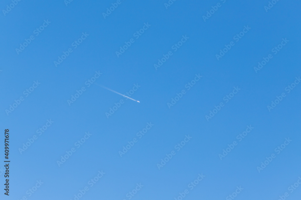 Blue sky without clouds. An airplane can be seen in the sky, followed by a flight trail. Blue sky without clouds. An airplane can be seen in the sky, followed by a flight trail.