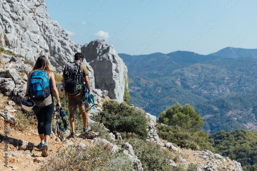 Full body back view of unrecognizable man and woman with backpacks and safety equipment walking on trail on rocky mountain slope Full body back view of unrecognizable man and woman with backpacks and safety equipment walking on trail on rocky mountain slope