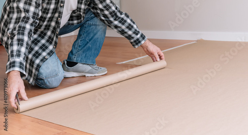 Crop unrecognizable male painter covering floor with craft paper while preparing room for painting and renovation