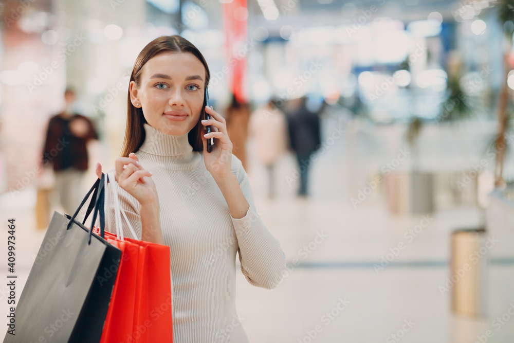 Positive young adult woman carrying paper shopping bags and mobile phone in hands Positive young adult woman carrying paper shopping bags and mobile phone in hands