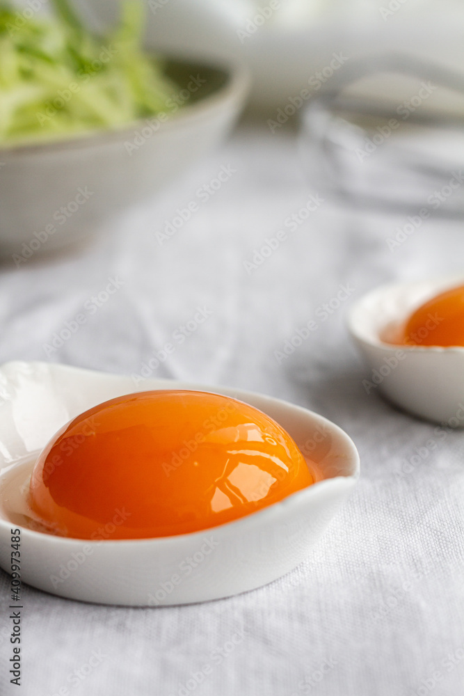 Ceramic bowls with separated raw egg yolks placed on table with fresh greens and mixer during breakfast preparation Ceramic bowls with separated raw egg yolks placed on table with fresh greens and mixer during breakfast preparation