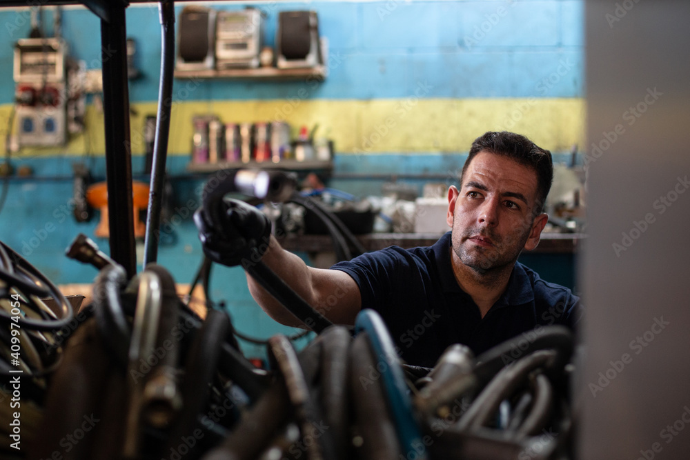Professional adult male mechanic taking hose for painting car from storage while working in repair service workshop Professional adult male mechanic taking hose for painting car from storage while working in repair service workshop
