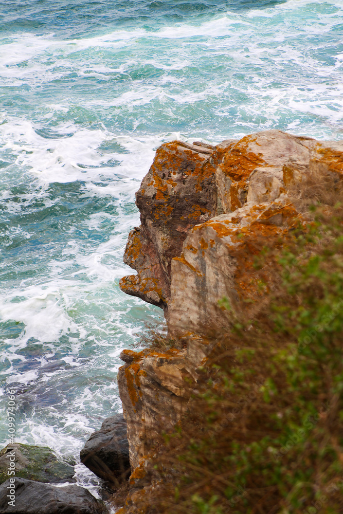 Side view of the brown part of the rock in the shape of a monkey against the background of a rough blue sea with large waves breaking on the rocks