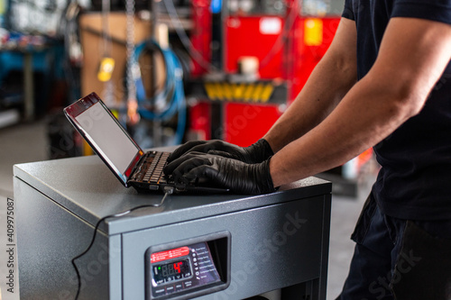 Adult man in using laptop to program broken machine during work in modern workshop