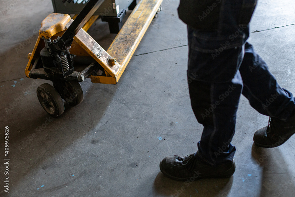 Side view of crop anonymous workman pulling trolley with heavy metal equipment while working in professional service workshop Side view of crop anonymous workman pulling trolley with heavy metal equipment while working in professional service workshop