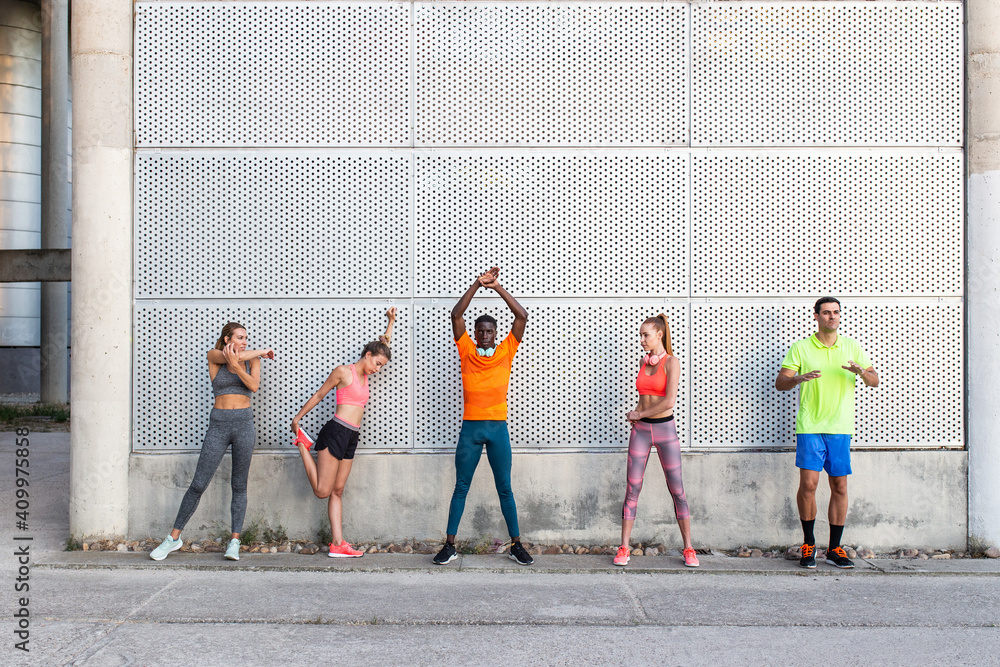 © Manuel Ruiz/ADDICTIVE STOCK - Group of multiracial runners in activewear standing in street and stretching muscles while preparing for training in city