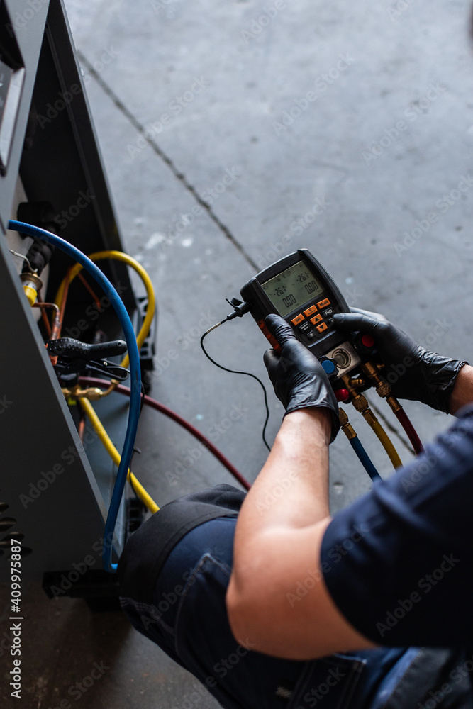 Crop of unrecognizable male mechanic in goggles and gloves using voltage tester on modern machine during work in workshop Crop of unrecognizable male mechanic in goggles and gloves using voltage tester on modern machine during work in workshop