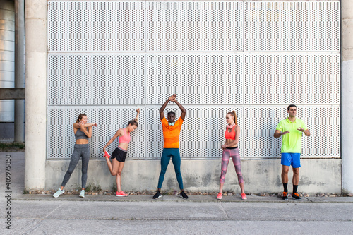 Group of multiracial runners in activewear standing in street and stretching muscles while preparing for training in city