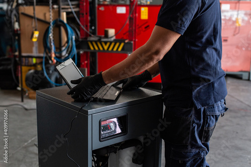 Unrecognizable adult man in using laptop to program broken machine during work in modern workshop photo