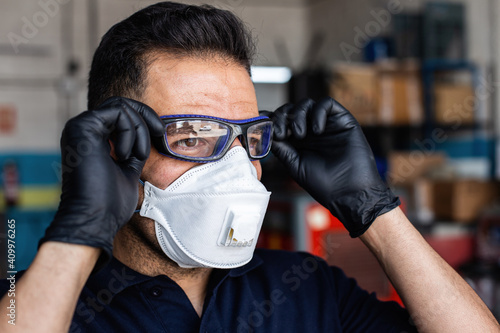 Adult man in latex gloves and respirator putting on protective goggles and looking at camera during work in garage photo