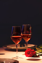 Beautiful table setting with glasses of wine and rose in dark room. Romantic dinner for Valentine's day