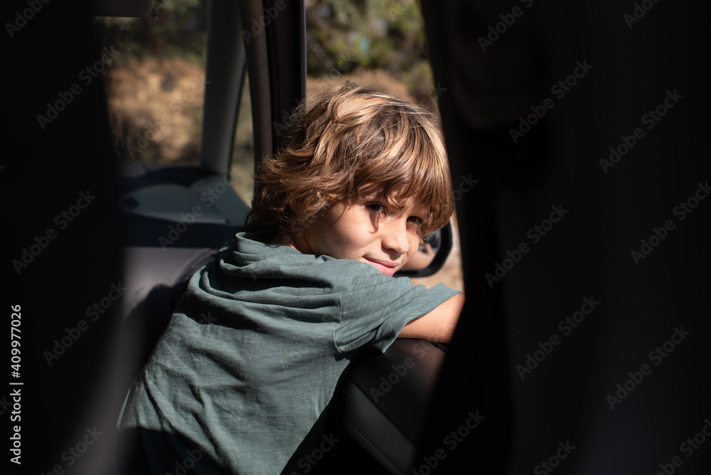 Side view of preteen boy with curly hair sitting in automobile looking out a window of while enjoying summer adventure in mountainous land Side view of preteen boy with curly hair sitting in automobile looking out a window of while enjoying summer adventure in mountainous land
