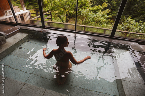Silhouette of young caucasian woman enjoying.a relaxing thermal waters bath at a traditional Japanese onsen ryokan, view from behind photo