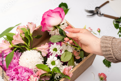 cropped view of woman holding pink flowers near wooden box on white