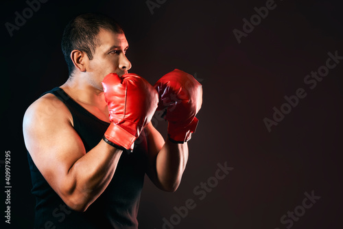 Hispanic male fighter is boxing and training with boxing gloves and is wearing a t-shirt that shows his strong and muscular arms. Isolated on black background with copy space