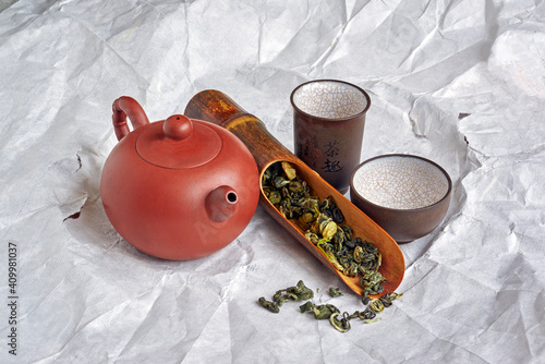 Chinese green  jasmine tea in the tea spoon with old clay traditional tea pot on white torn,  wrapping old paper background close up