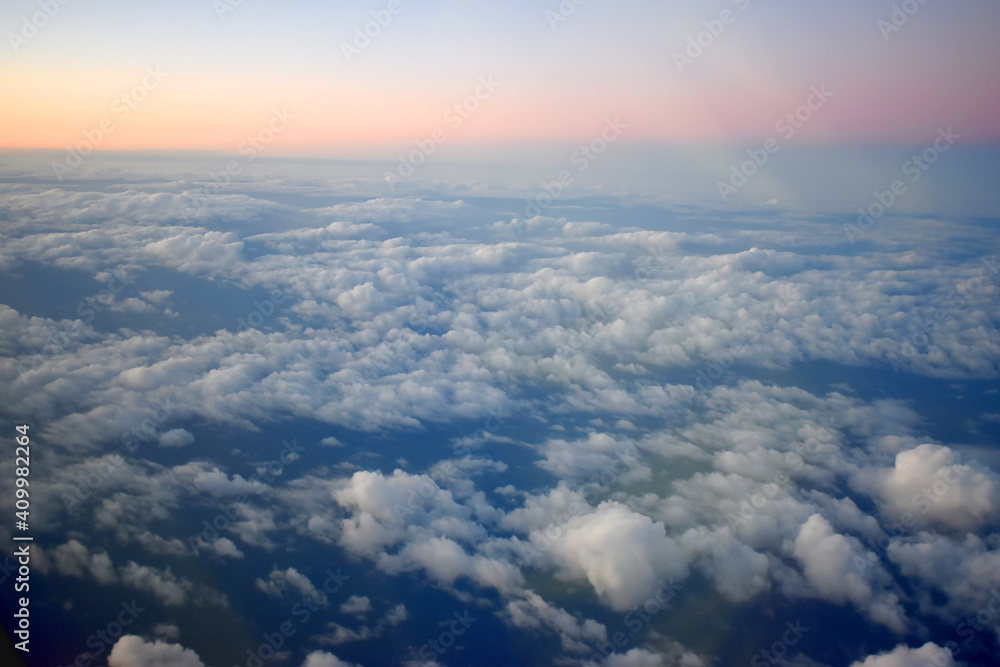  Beautiful orange color of horizon in blue sky with white clouds floating on sunset sky. Viewed from airplane window.