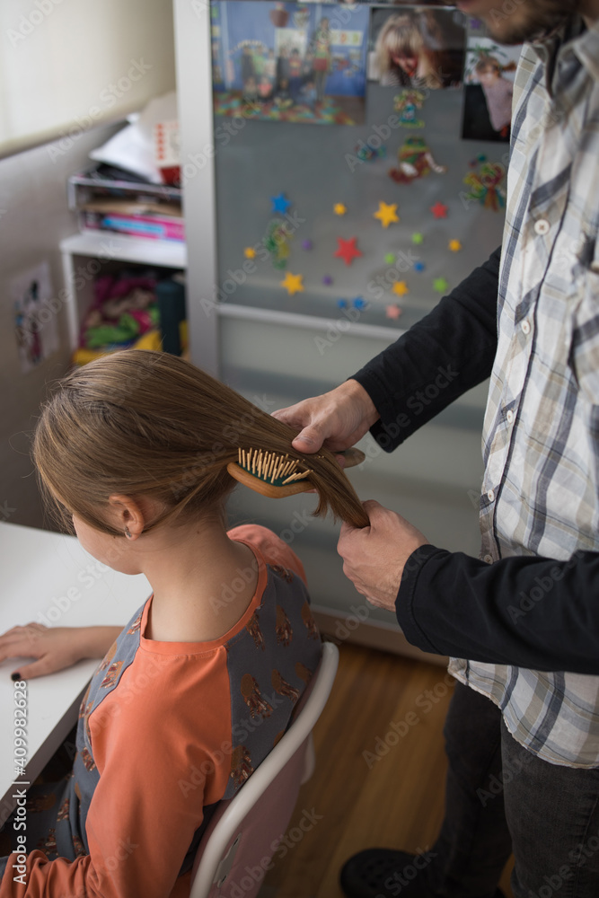 Side view of cropped unrecognizable positive adult man brushing long hair of preteen daughter with hairbrush during daily routine at home Side view of cropped unrecognizable positive adult man brushing long hair of preteen daughter with hairbrush during daily routine at home